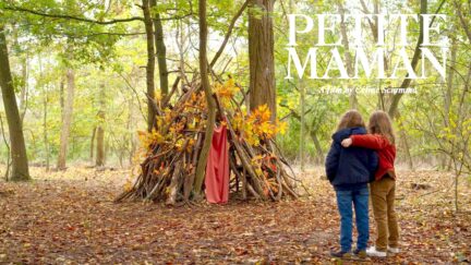 在Celine Sciamma的《Petite Maman》中，两个女孩在观察他们在树林中搭建的避难所时相互拥抱。